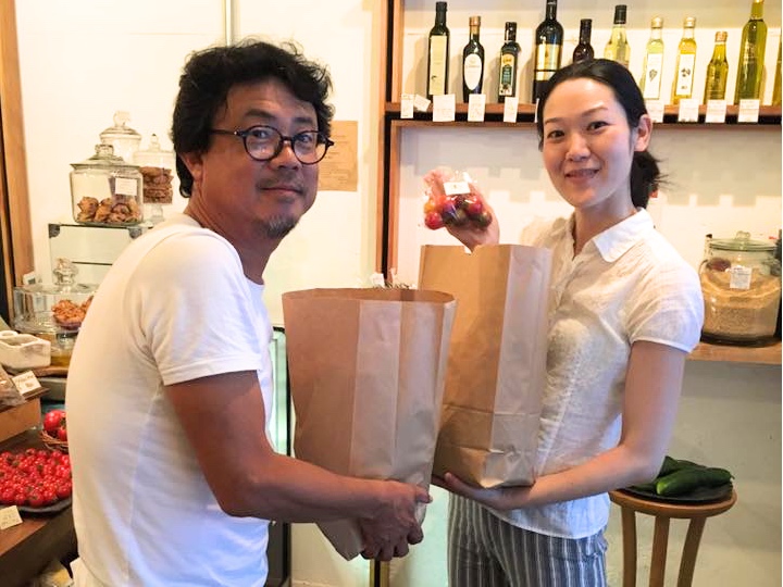 「ごちそうじかん」主催の山崎さん（右）に野菜を渡す大皿さん。ピックアップステーションにて。